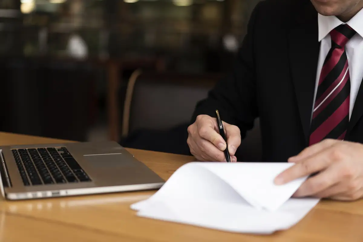 Advogado revisando e assinando documentos ao lado do computador