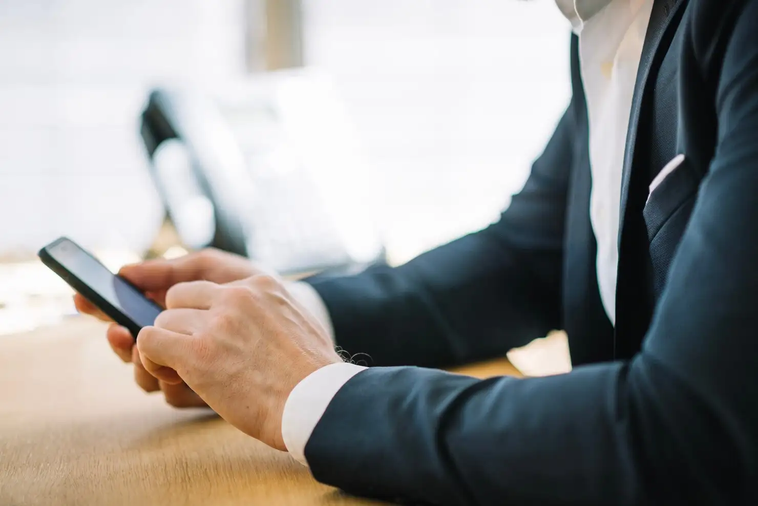 Profissional de terno usando o celular em uma mesa de trabalho
