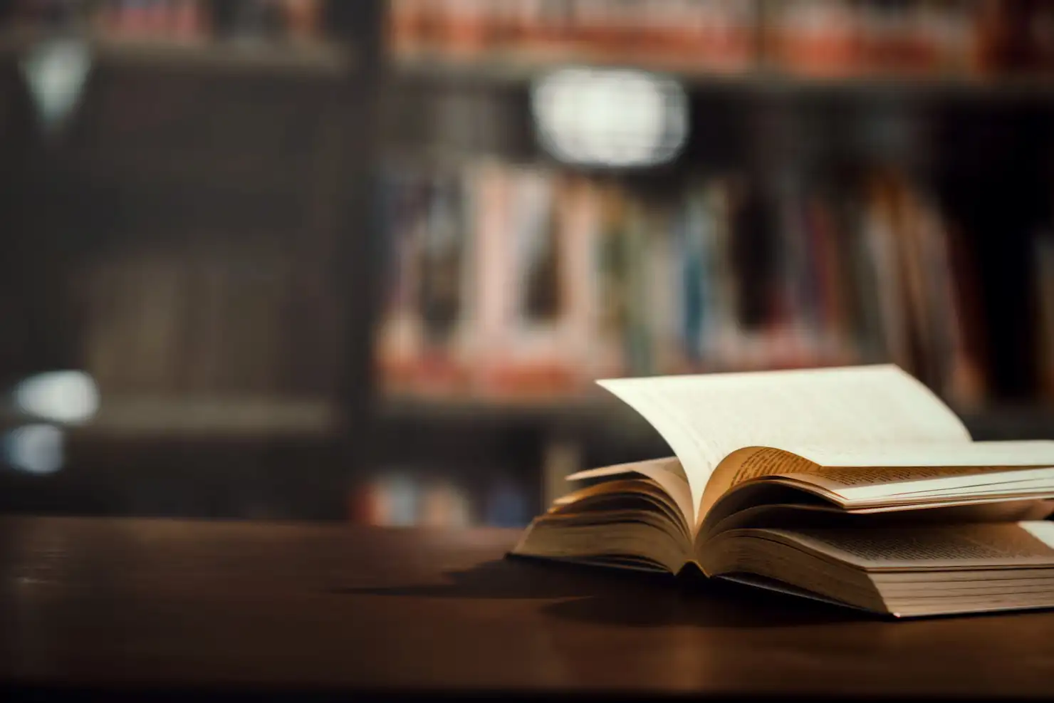Livro aberto sobre a mesa, diante de uma estante de biblioteca